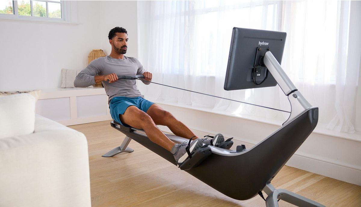 Rowing machine with a man exercising indoors, featuring a large display and sleek design.