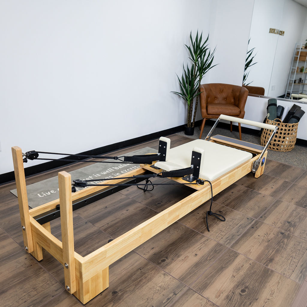 Reformer Pilates machine with a wooden frame and padded platform in a bright studio.