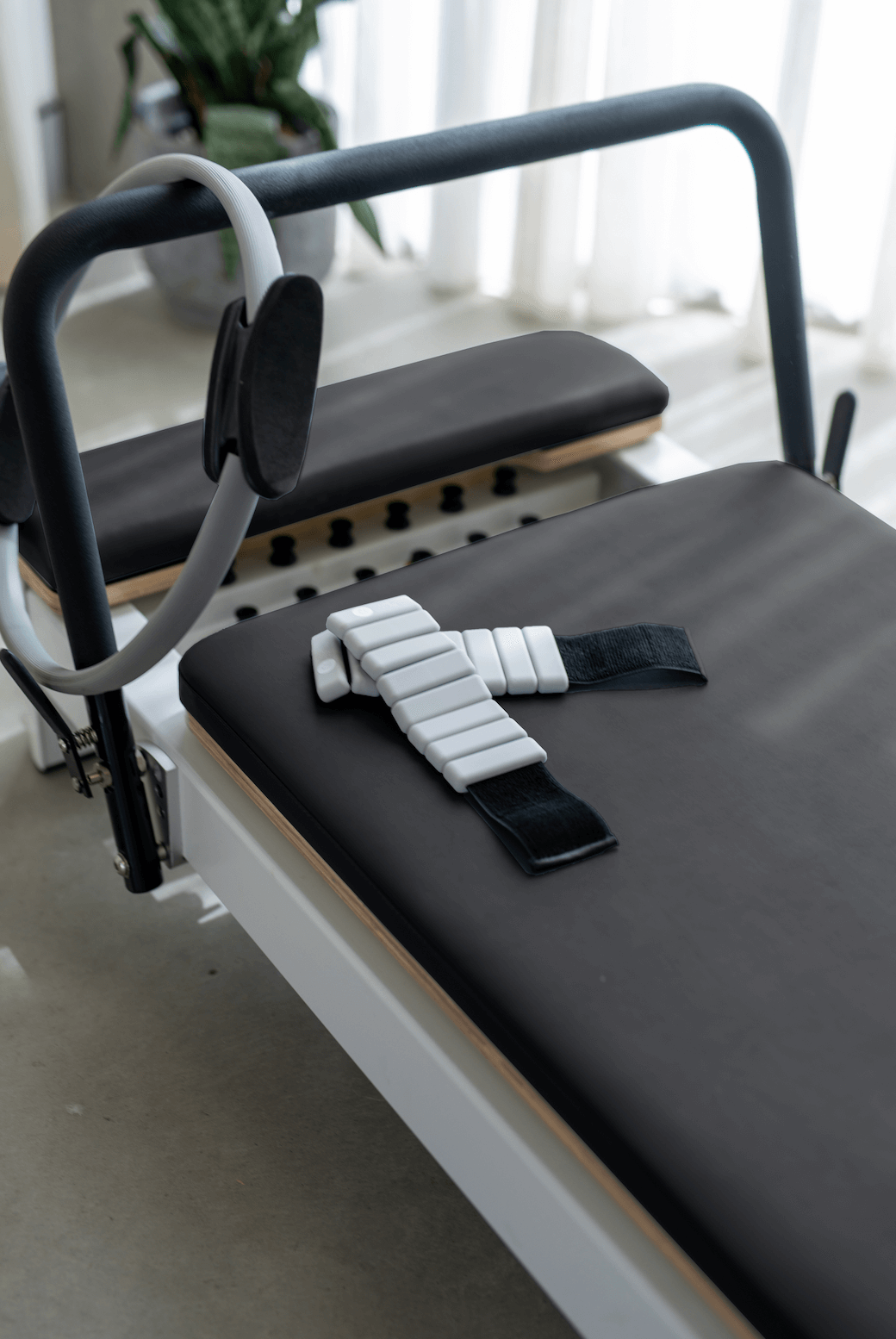 Reformer Pilates machine with black padded surface and adjustable straps.