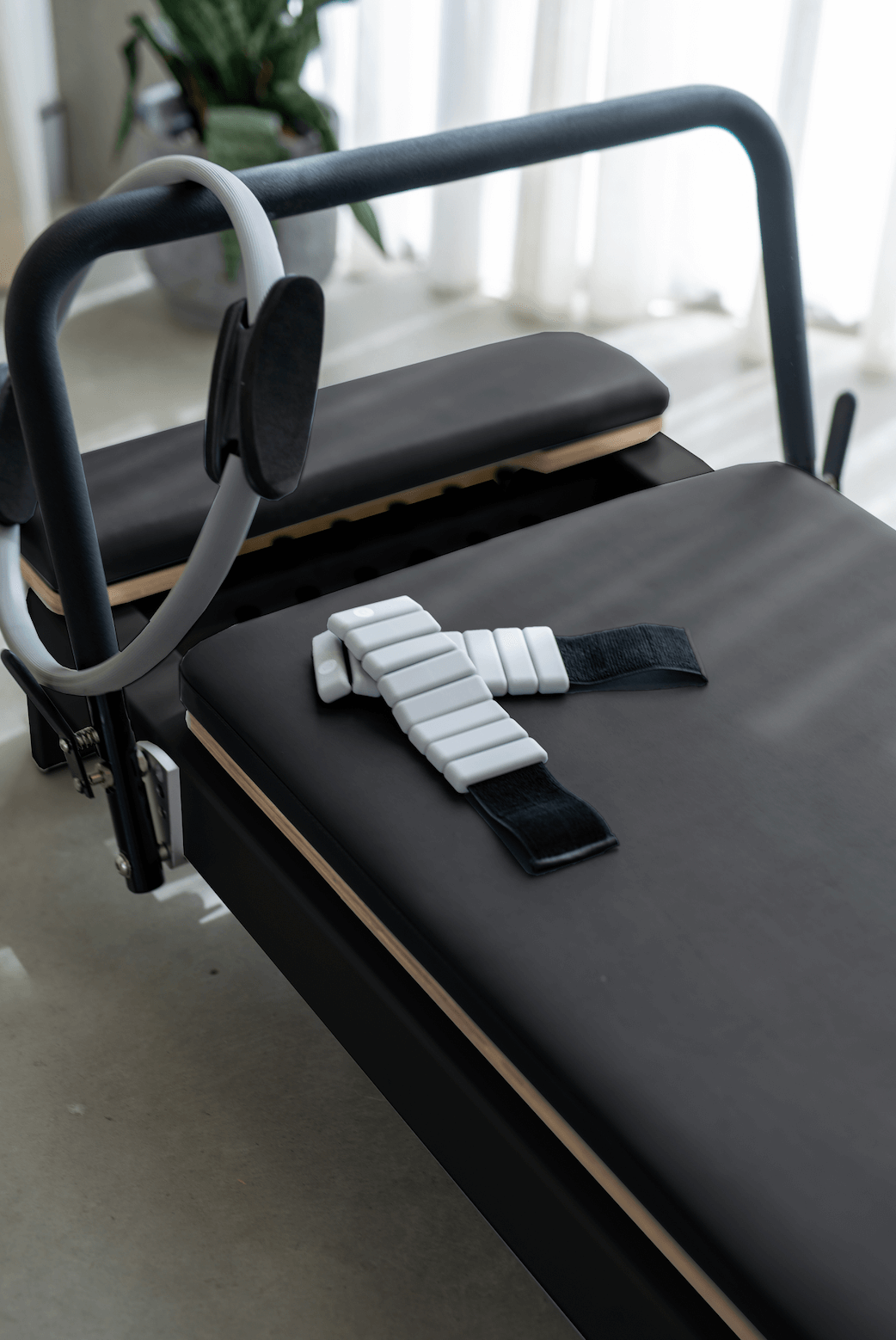 Pilates reformer with black padded surface and adjustable straps for workouts.