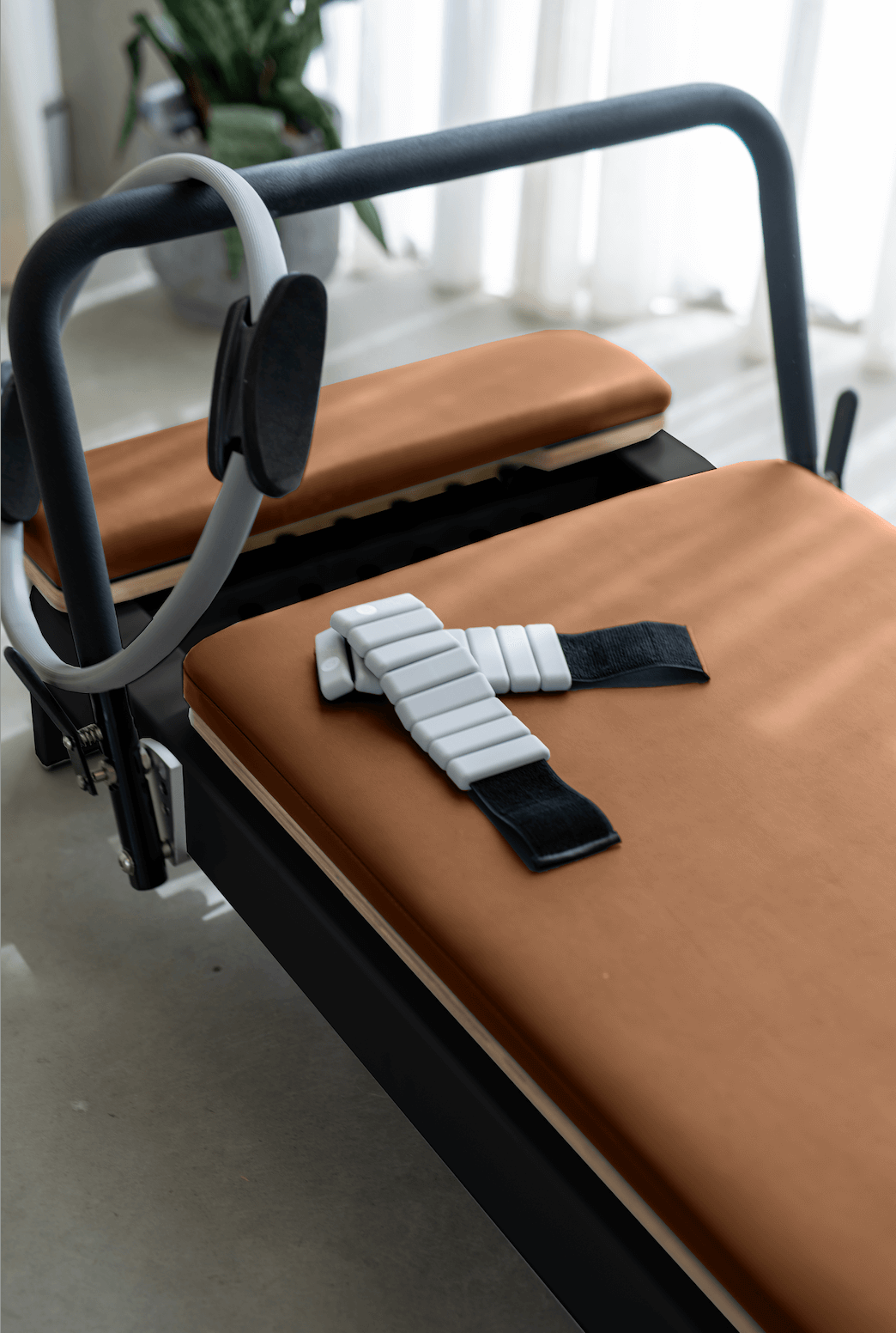Pilates reformer with brown padding and adjustable straps for resistance training.