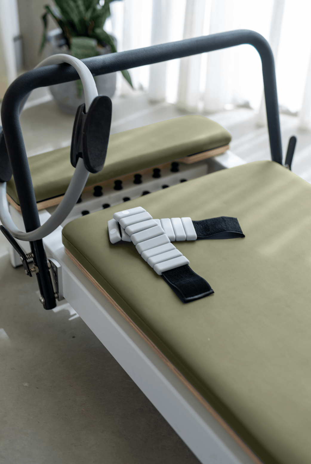 Reformer Pilates machine with green cushion and adjustable straps for workouts.