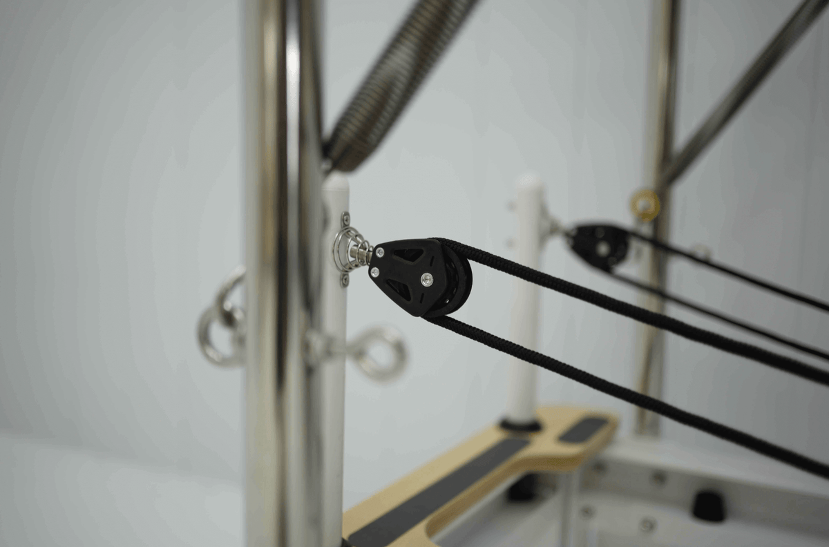 Pilates reformer pulley system with black straps and silver frame details.