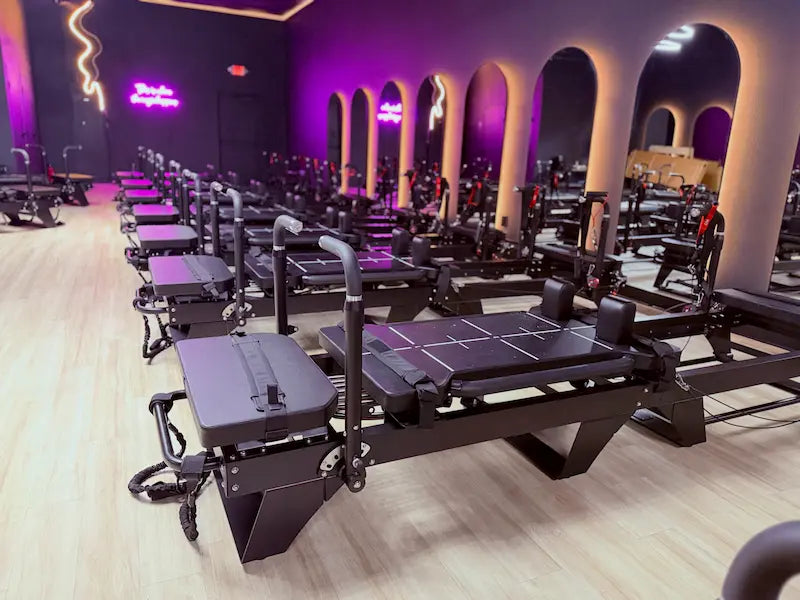 Reformer Pilates machine setup in a modern studio with purple lighting.