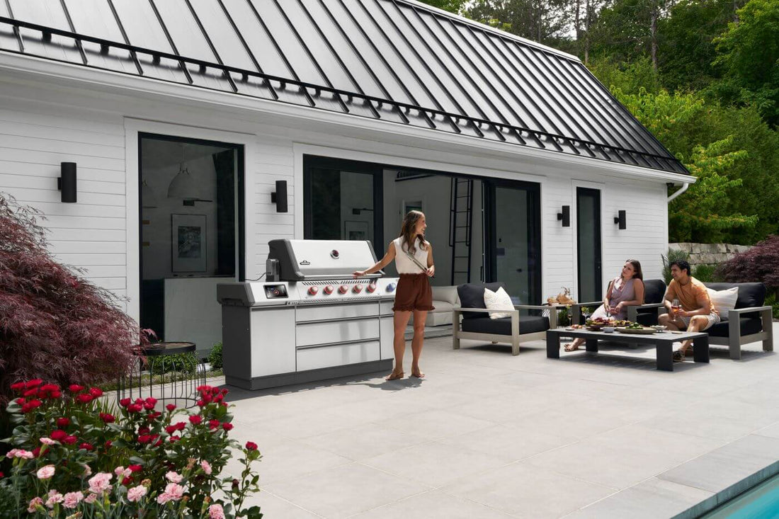Freestanding stainless gas grill on a patio beside a house