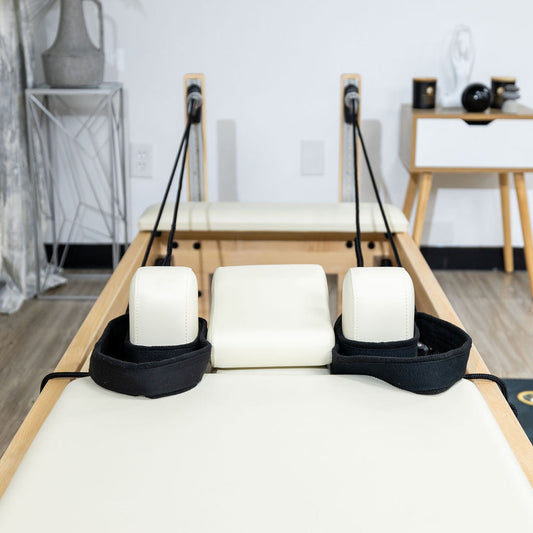 Pilates reformer with padded headrest and adjustable straps in a modern studio setting.