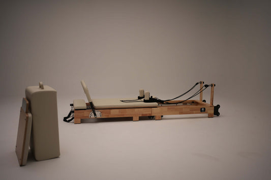 Reformer Pilates machine with wooden frame and padded surface for exercise.